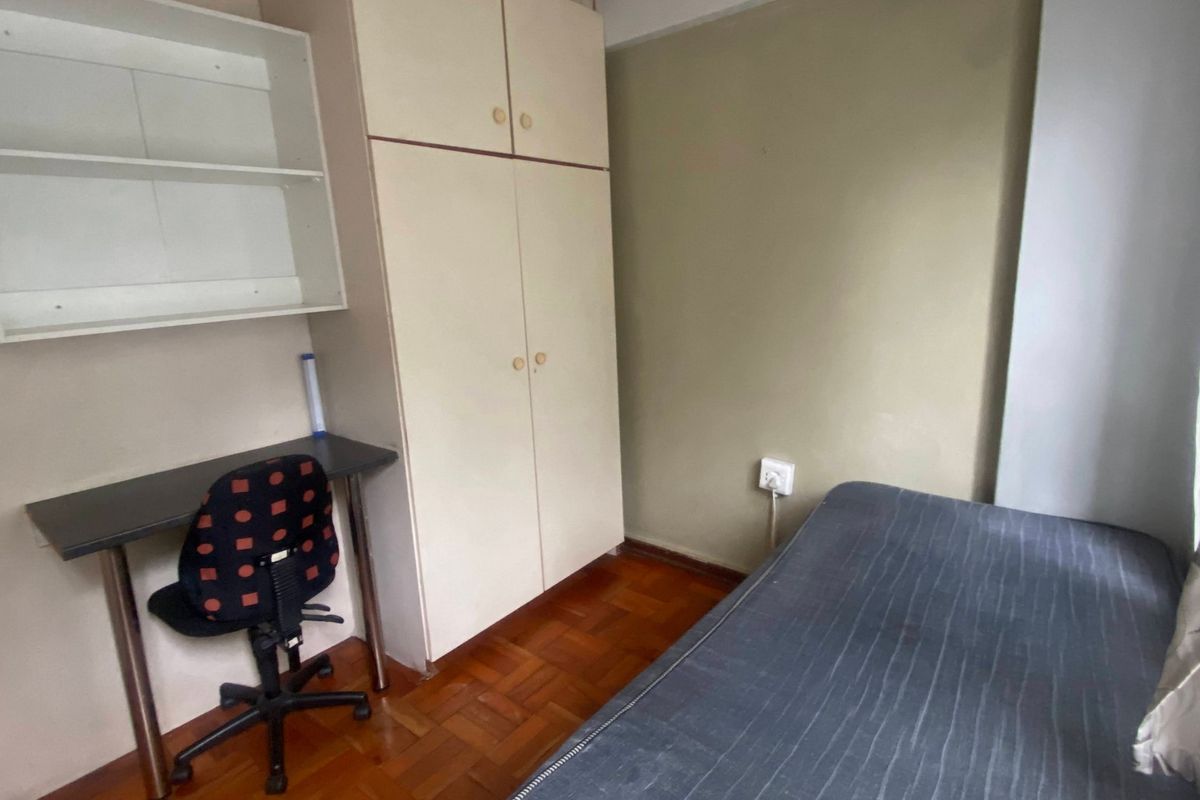 A compact bedroom featuring parquet flooring, a built-in wardrobe, and wall-mounted shelving, offering a functional space with potential for cosmetic updates.