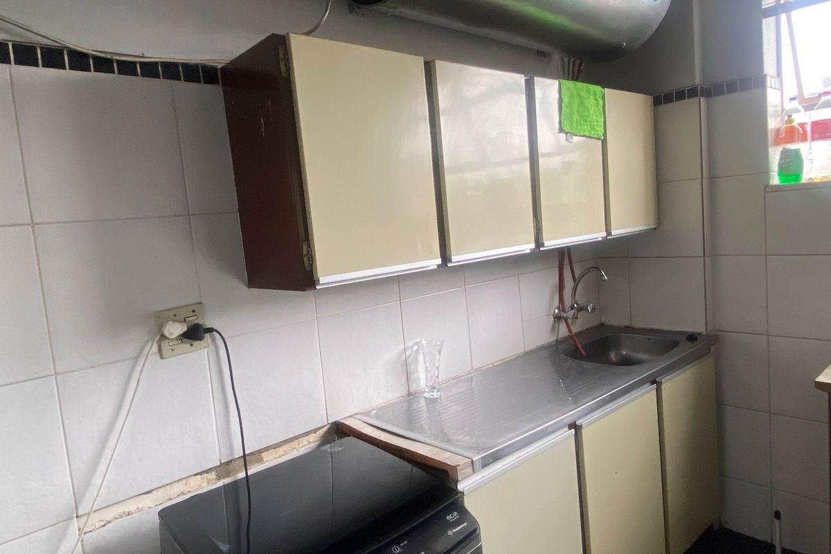 A compact kitchen area featuring dated cabinetry, a stainless steel sink, and tiled walls, requiring modernization to improve functionality and aesthetic appeal.