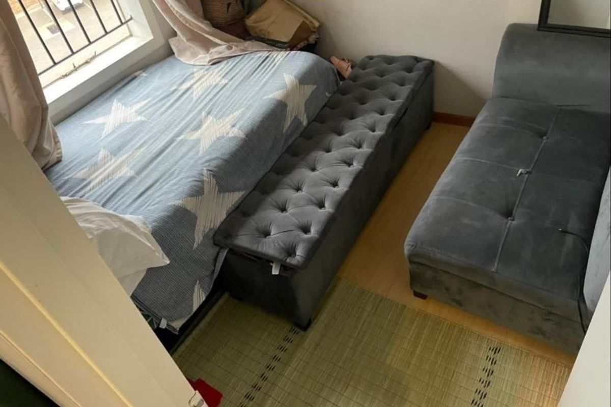 A compact bedroom featuring laminate flooring and a window fitted with security bars.