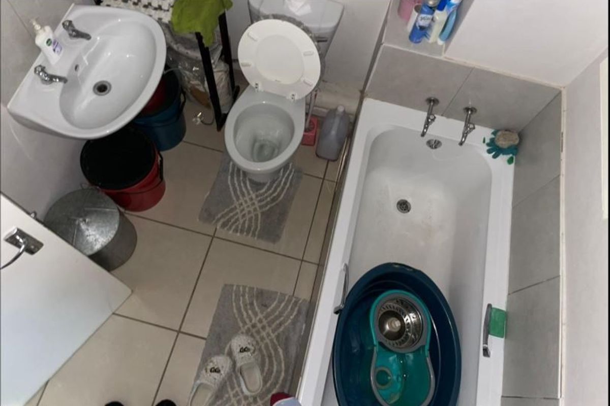 A compact bathroom featuring a pedestal basin, toilet, and bathtub with tiled finishes, requiring cosmetic updates to improve its overall condition.