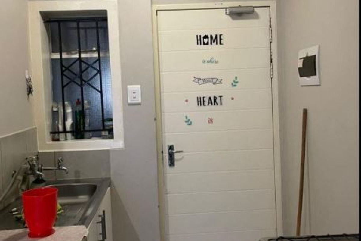 A compact kitchen area featuring a stainless steel sink, gas stove, and tiled flooring with security bars on the window.