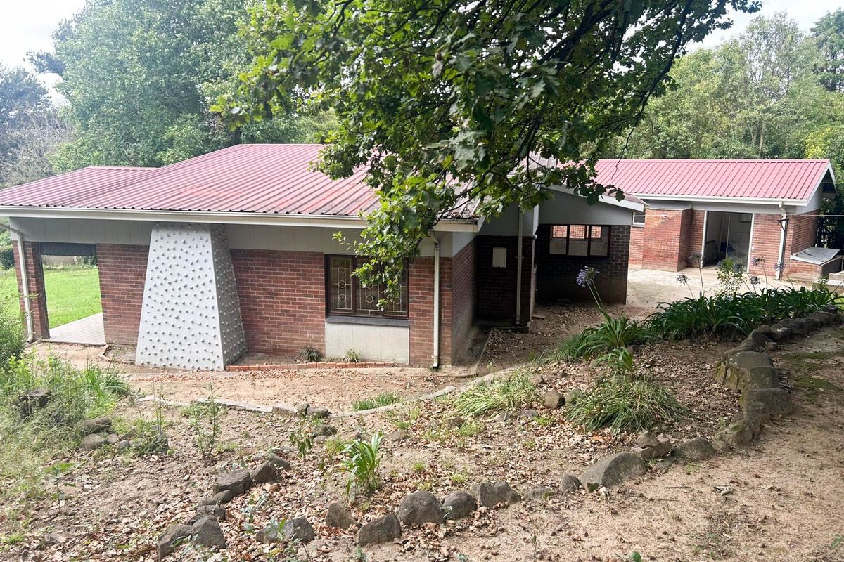 Rear view of a brick house featuring a corrugated metal roof, security-barred windows, and a sloped garden with stone edging.