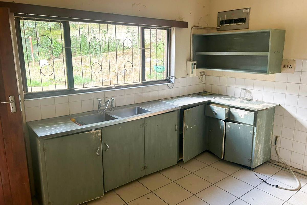 A dated kitchen featuring original cabinetry, a stainless steel sink, and tiled flooring, requiring renovation to modernize the space.
