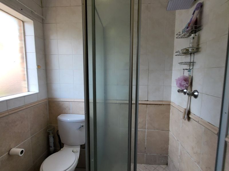 A functional bathroom featuring a shower enclosure, toilet, and tiled finishes, requiring some cosmetic updates to refresh the space.