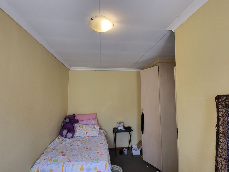 A compact bedroom featuring a built-in wardrobe, neutral wall finishes, and a central ceiling light fixture.