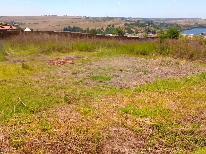 A vacant residential plot featuring natural grass coverage and a perimeter boundary wall, offering scenic landscape views.