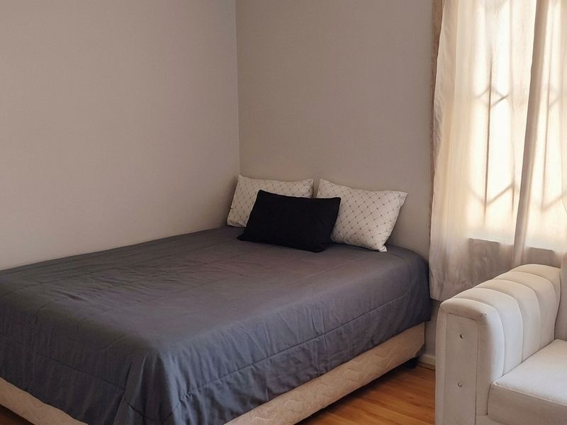 A functional bedroom featuring laminate flooring and natural light through a window with security bars.