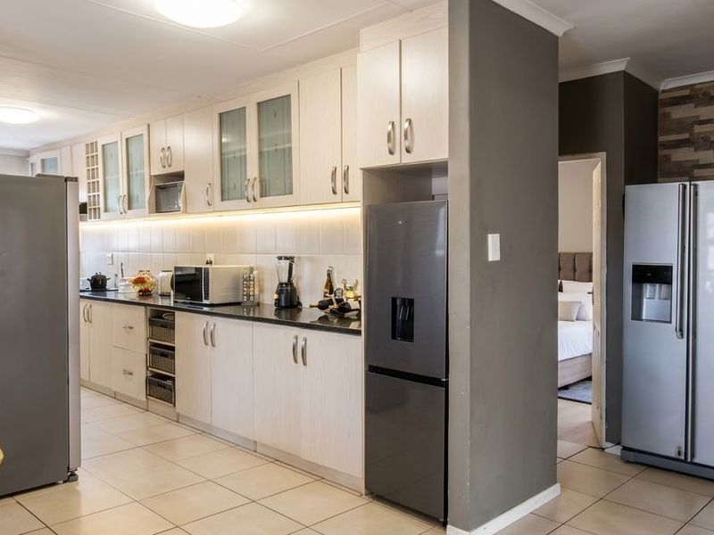 A functional kitchen featuring light-toned cabinetry, dark countertops, tiled flooring, and integrated under-cabinet lighting, providing a clean and practical workspace.
