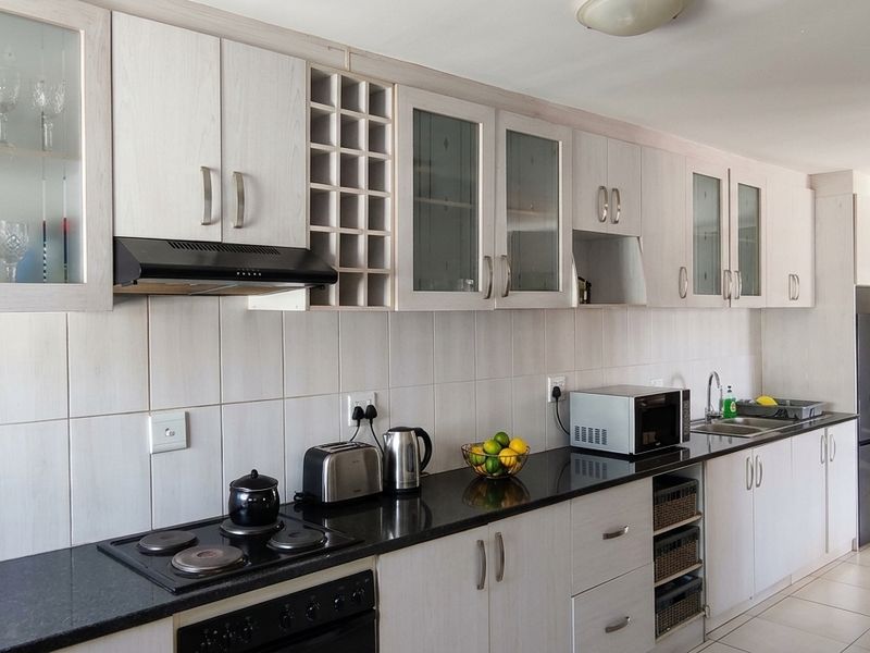 A functional kitchen featuring light wood-grain cabinetry, black granite countertops, a built-in electric hob, extractor fan, and tiled backsplash.