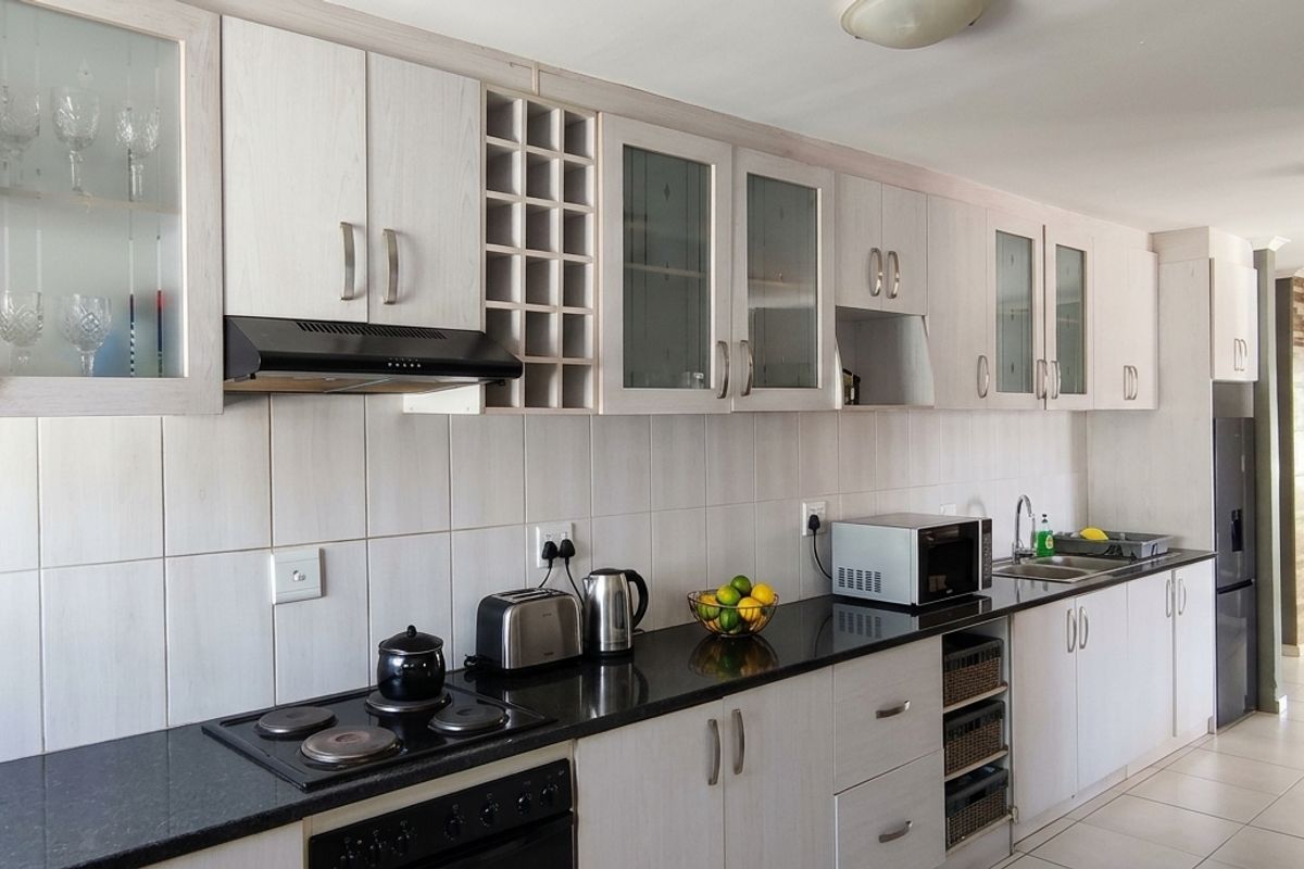 A functional kitchen featuring light wood-grain cabinetry, black granite countertops, a built-in electric hob, extractor fan, and tiled backsplash.