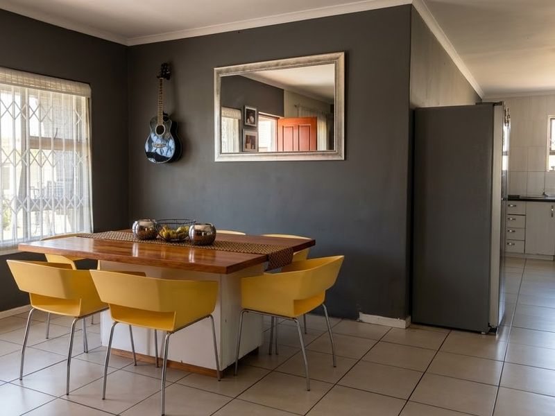 Open-plan dining area flowing into a functional kitchen with tiled flooring, built-in cabinetry, and security gates on windows.