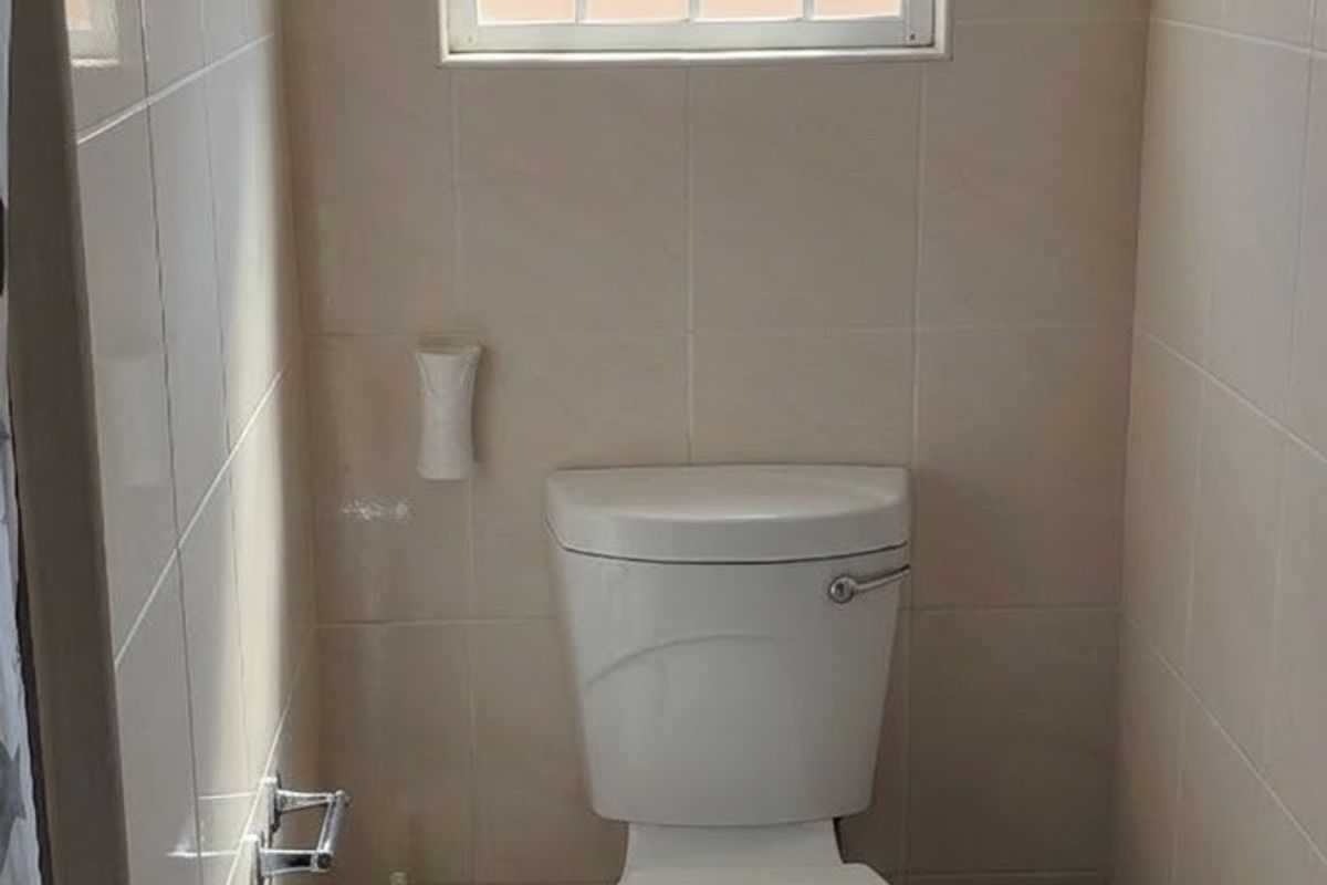 A compact bathroom featuring tiled walls, tiled flooring, and a window fitted with a security gate.