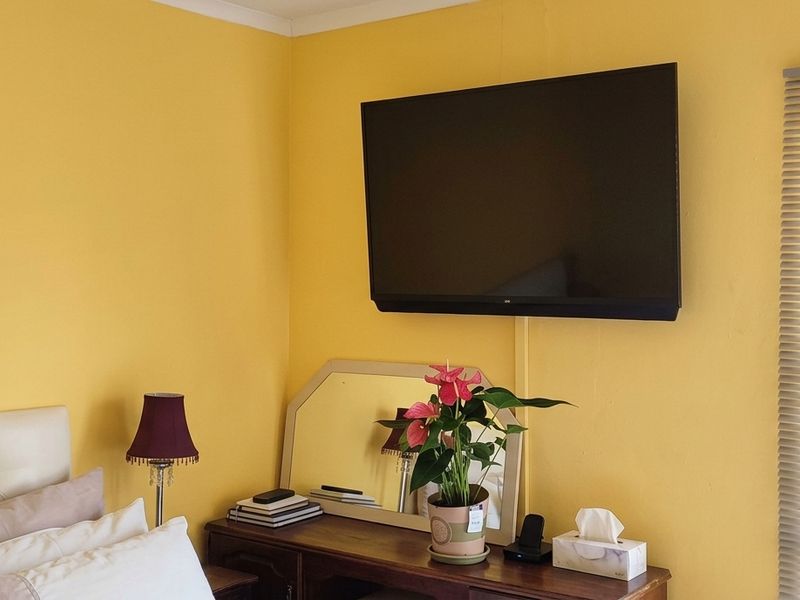A bedroom featuring yellow walls, a wall-mounted television, and venetian blinds on the window.