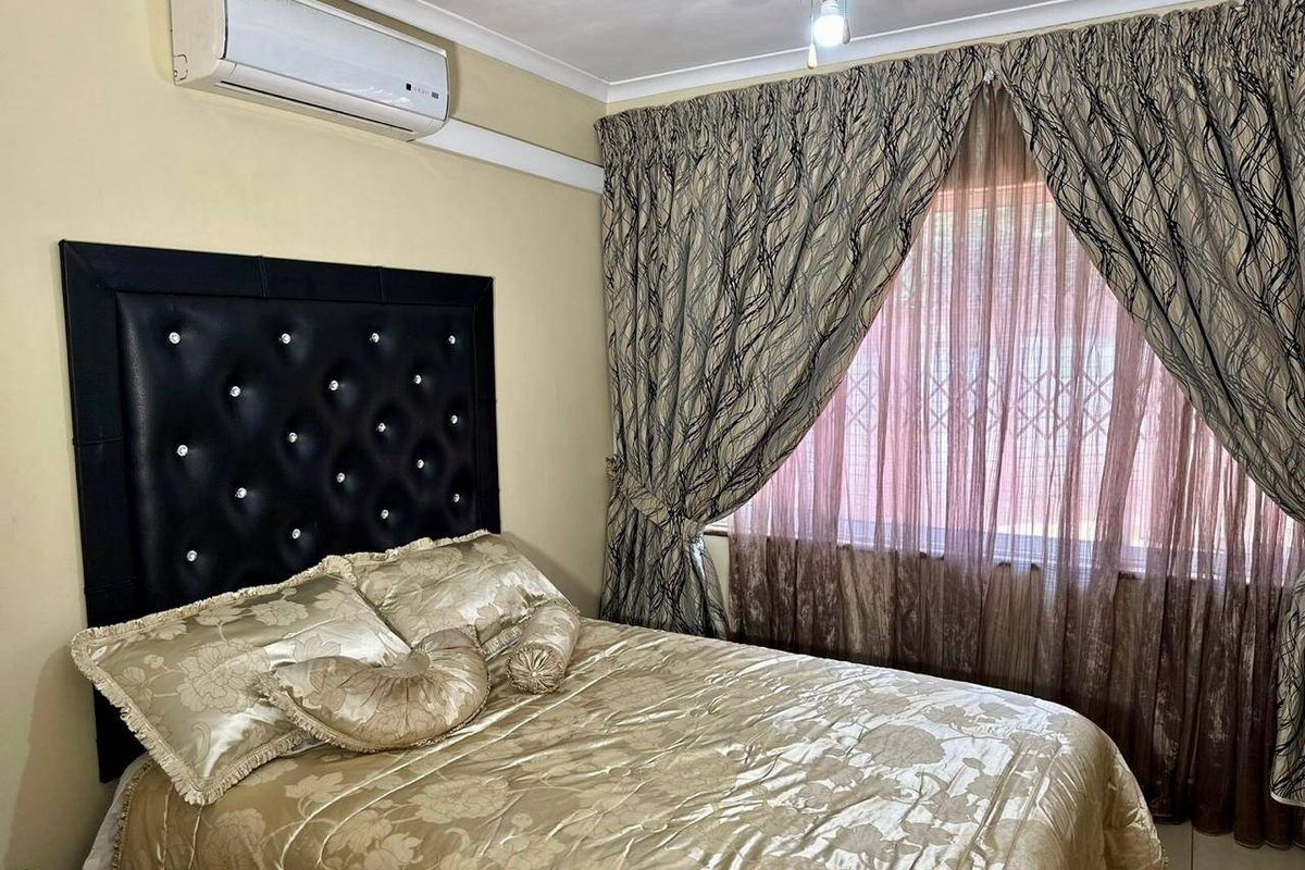 A bedroom featuring a wall-mounted split-system air conditioner, cove cornicing, and security bars on the window.