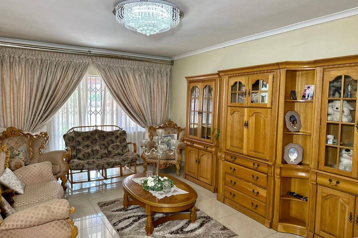 A well-maintained living room featuring large format floor tiles, a decorative crystal chandelier, and large windows with security gates.