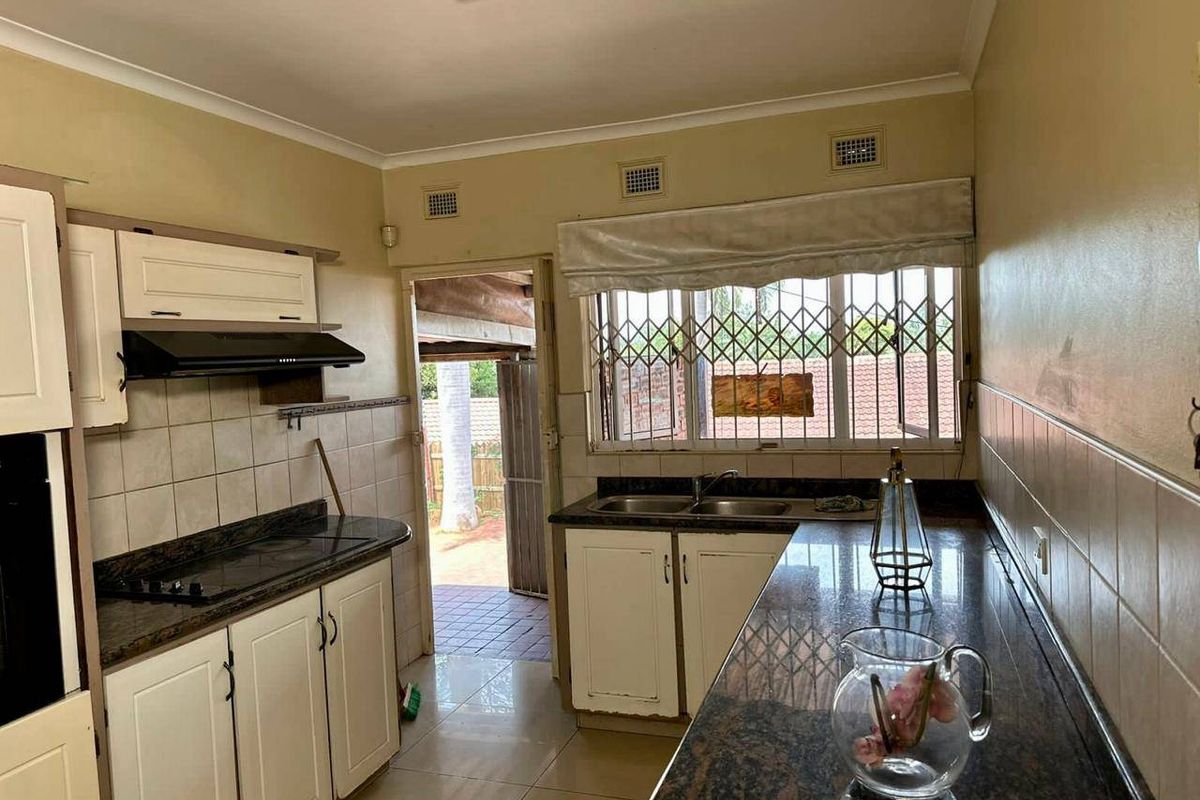 A functional kitchen featuring granite countertops, a double basin sink, and built-in cooking appliances, with direct access to an outdoor patio area.