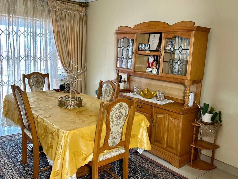 A formal dining room featuring tiled flooring, a decorative crystal chandelier, and a sliding glass door with an integrated security gate.