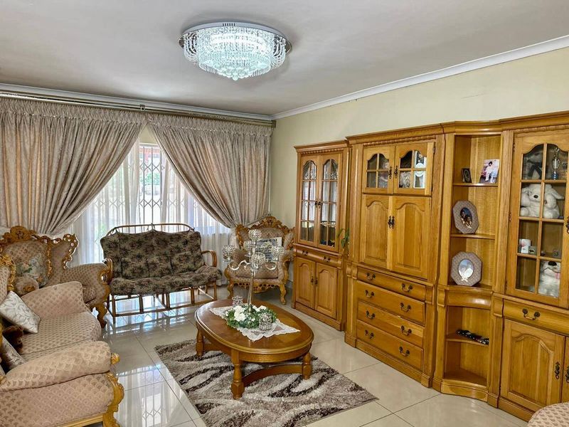 A well-maintained living room featuring large format floor tiles, a decorative crystal chandelier, and large windows with security gates.