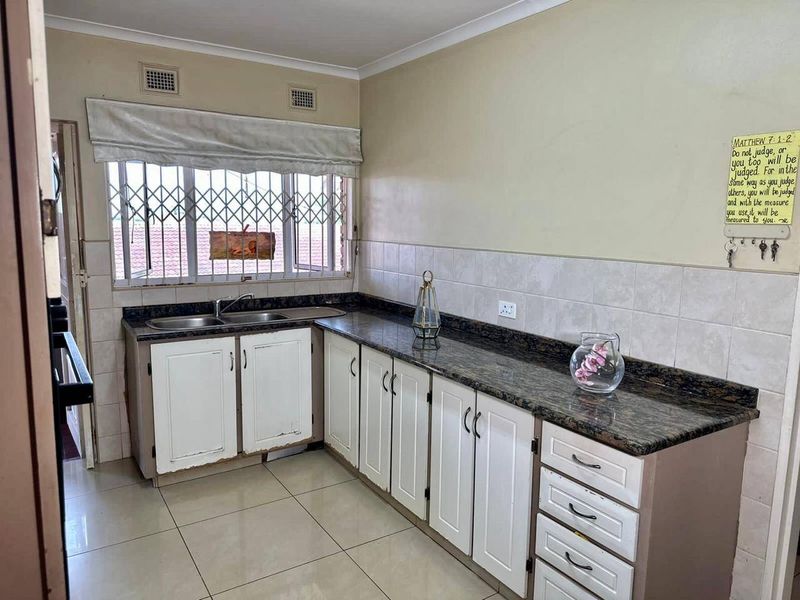 A functional kitchen featuring granite countertops, tiled backsplash, and ample built-in cabinetry, with ceramic floor tiles throughout.