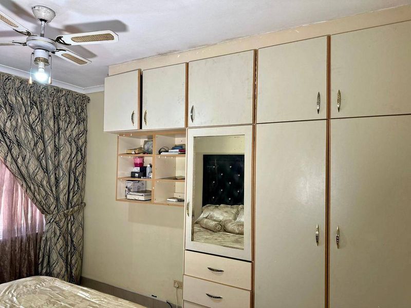Bedroom featuring extensive built-in cabinetry with integrated mirror and a ceiling fan, showing signs of wear and dated finishes.