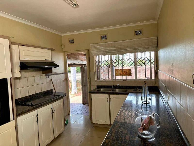 A functional kitchen featuring granite countertops, a double basin sink, and built-in cooking appliances, with direct access to an outdoor patio area.