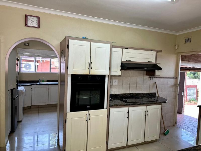 A functional kitchen featuring built-in oven, hob, extractor fan, granite countertops, and tiled splashbacks, with an adjacent scullery area visible through the archway.