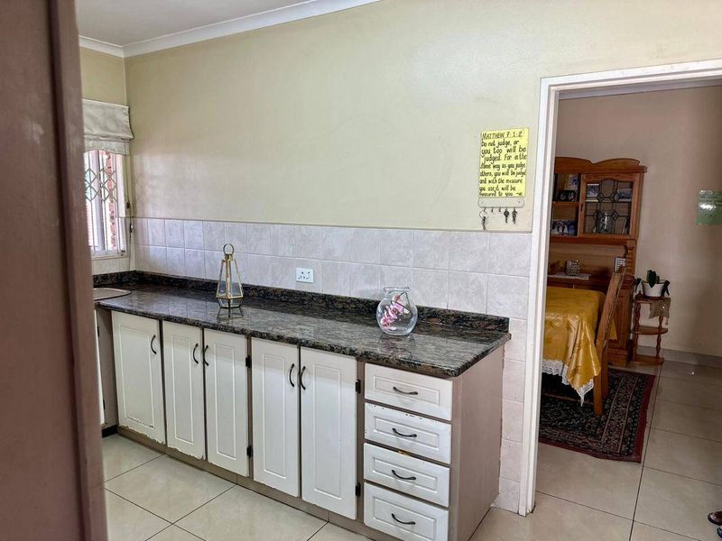 A functional kitchen featuring granite countertops, tiled backsplash, and white cabinetry, with ceramic floor tiles throughout.