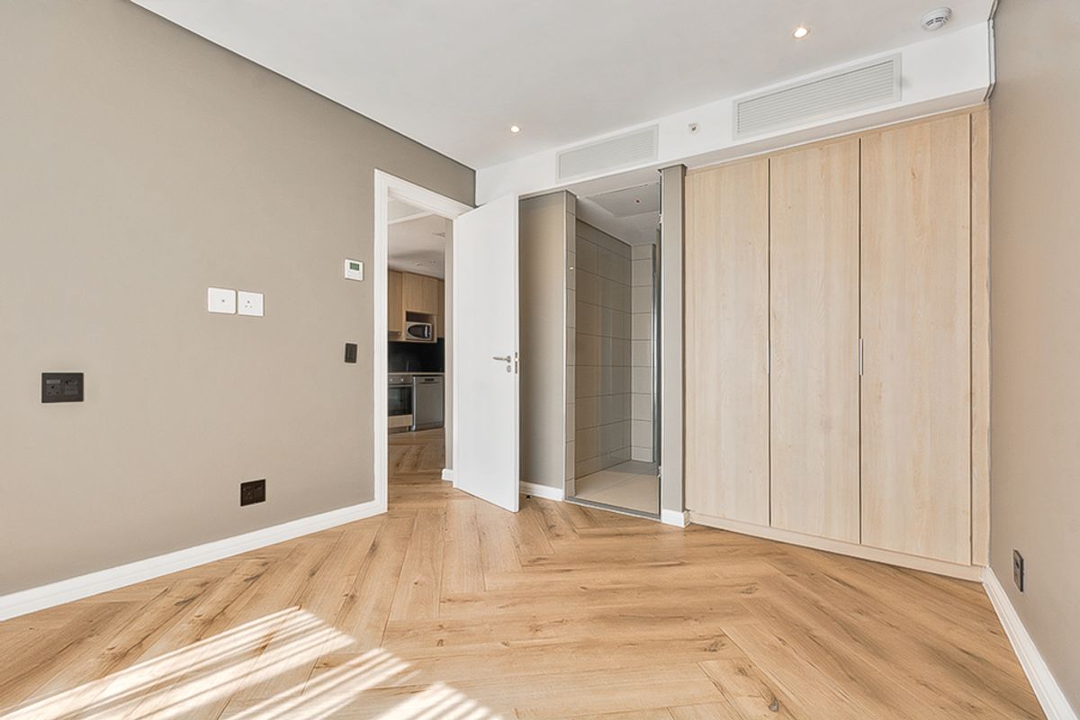 Modern bedroom featuring light wood herringbone flooring, built-in wardrobes, recessed lighting, and direct access to an en-suite bathroom.