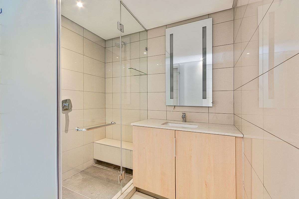 Modern bathroom featuring a glass-enclosed shower with a built-in bench, grab bar, and a sleek vanity with an integrated sink and mirror.