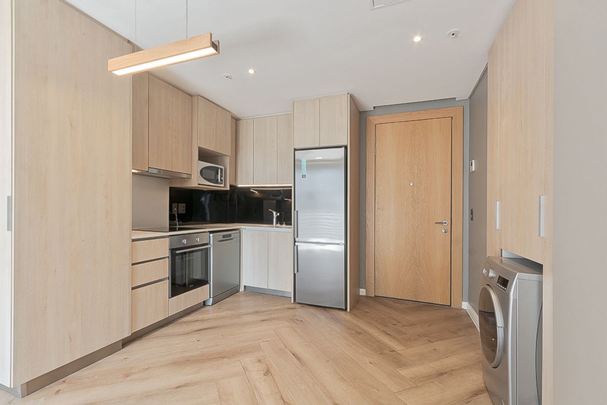Modern open-plan kitchen featuring light-wood cabinetry, integrated appliances, herringbone flooring, and a dedicated laundry cupboard, creating a seamless and functional living space.