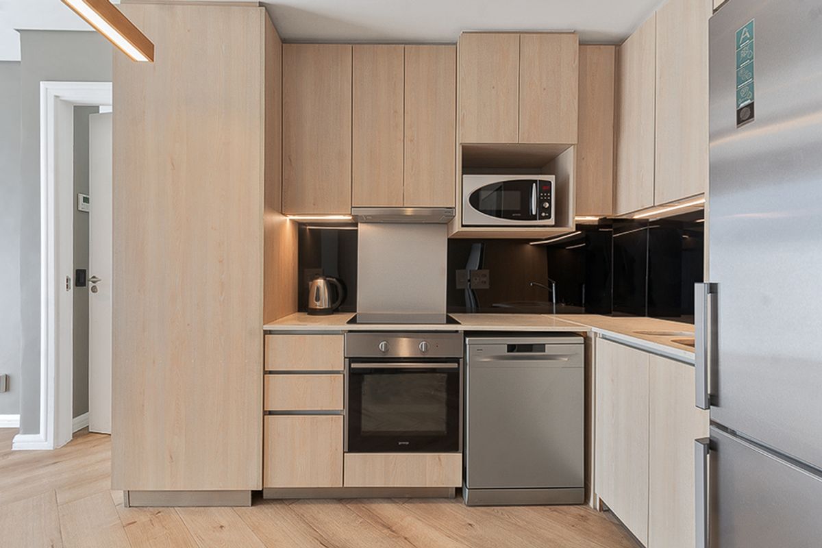 Modern kitchen featuring light-wood cabinetry, integrated appliances, a sleek black glass splashback, and high-quality engineered wood flooring.