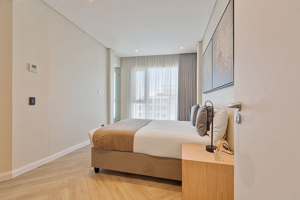 A modern, well-maintained bedroom featuring elegant herringbone flooring, recessed lighting, and large windows with floor-to-ceiling curtains.