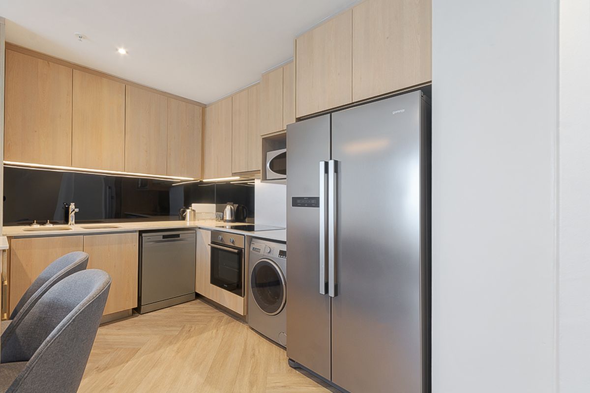 Modern kitchen featuring light wood cabinetry, integrated appliances, sleek dark splashback, and herringbone flooring, offering a clean and contemporary aesthetic.