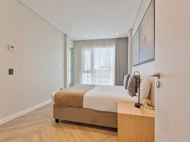 A modern, well-maintained bedroom featuring elegant herringbone flooring, recessed lighting, and large windows with floor-to-ceiling curtains.