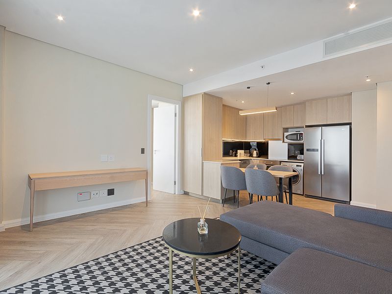 Modern open-plan living area featuring herringbone flooring, recessed lighting, and a sleek kitchen with integrated appliances and light wood cabinetry.