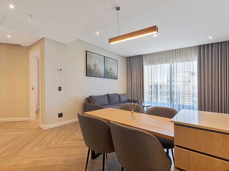 Modern open-plan living and dining area featuring herringbone flooring, contemporary pendant lighting, and seamless access to a private balcony.