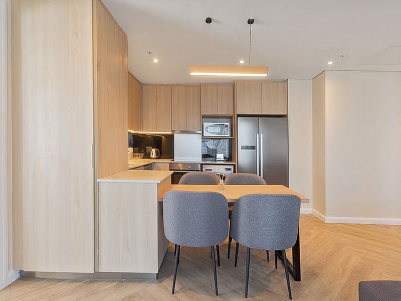 Modern open-plan kitchen featuring light oak cabinetry, integrated appliances, and elegant herringbone wood flooring, creating a seamless and contemporary living space.
