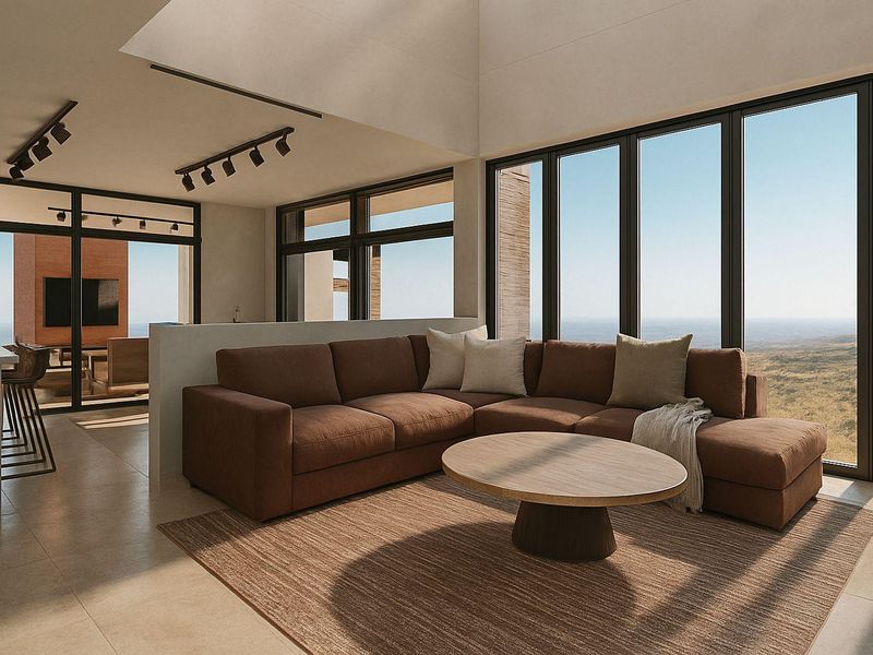 Modern open-plan living area featuring vaulted ceilings, track lighting, and expansive floor-to-ceiling windows with panoramic landscape views.