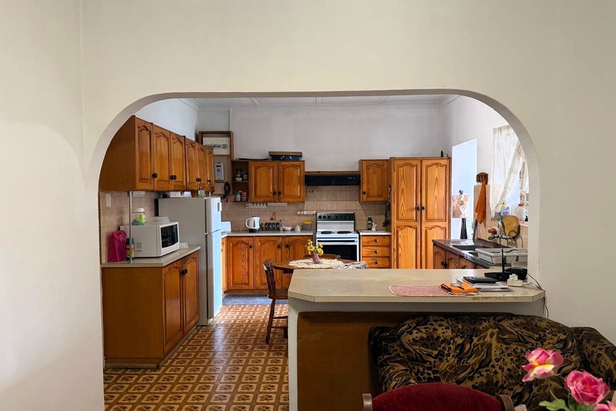 A dated kitchen featuring traditional wooden cabinetry, laminate countertops, and a freestanding oven, connected to the living area via a classic archway.