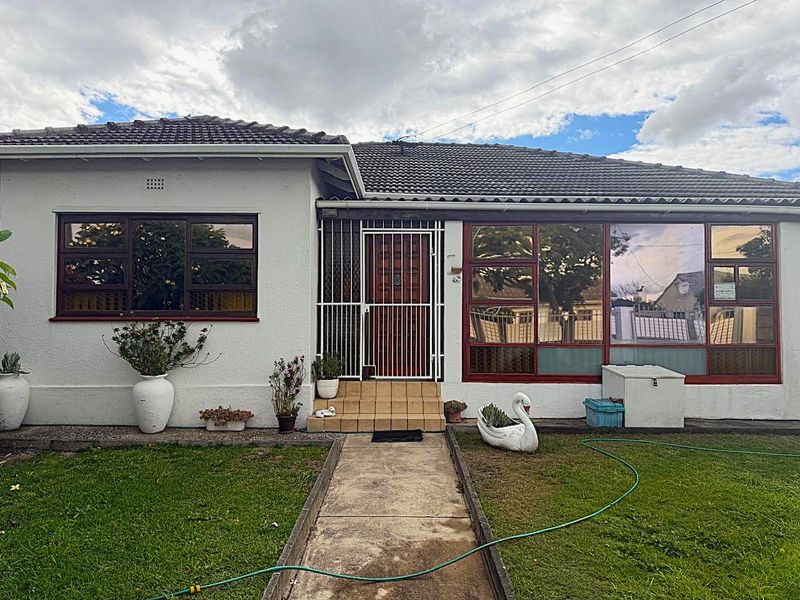 Front elevation of a single-story house featuring a tiled roof, concrete walkway, and security gate entrance with aluminium window frames.