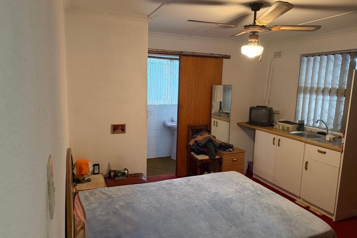A bedroom featuring a kitchenette area with built-in cabinetry, a sink, and an attached bathroom with a sliding door entry.