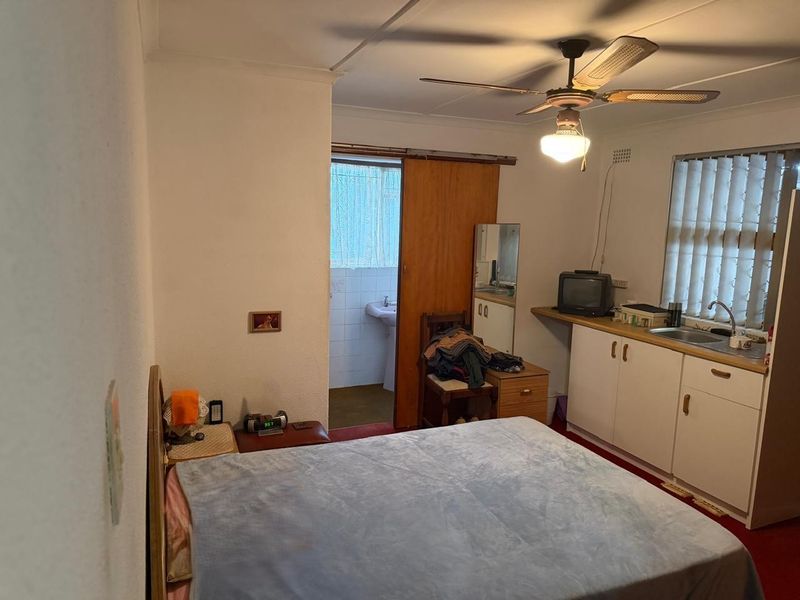 A bedroom featuring a kitchenette area with built-in cabinetry, a sink, and an attached bathroom with a sliding door entry.