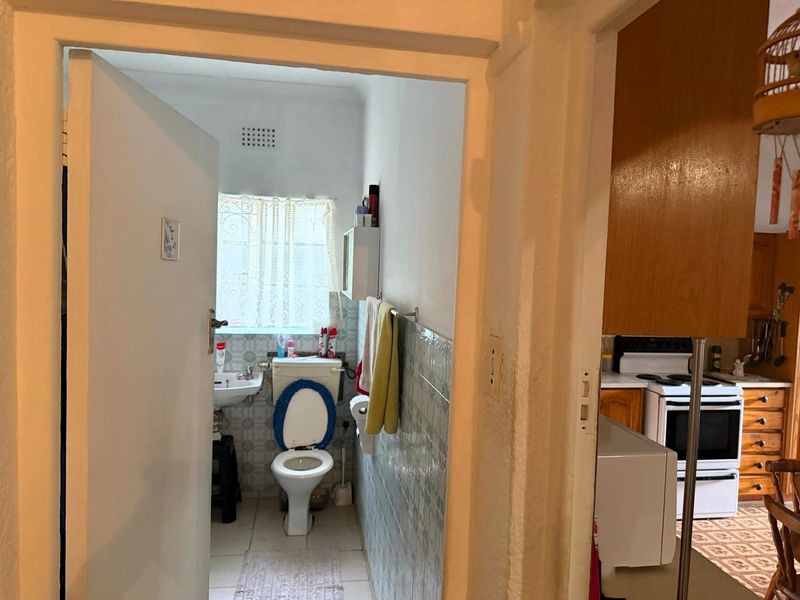 A functional bathroom featuring a pedestal basin and toilet, with tiled walls and flooring. The space is dated and would benefit from modernization.