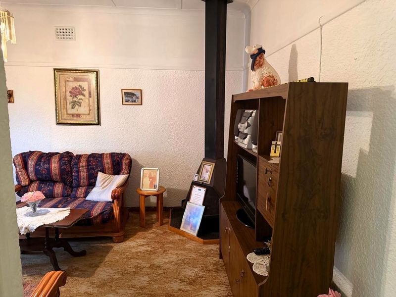 A living room featuring a freestanding fireplace, textured walls, and coved ceilings, offering a dated interior space ready for modernization.
