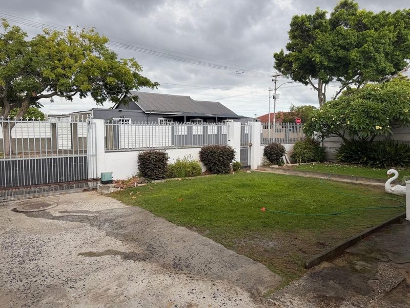 Front exterior view of the property featuring a gated entrance, perimeter wall, concrete driveway, and a well-maintained front lawn and garden area.