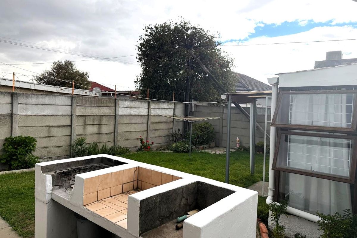 Rear garden featuring a built-in braai area, lawn, and precast concrete boundary wall with security fencing.