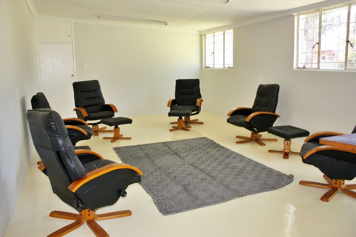 A spacious, neutral living area featuring tiled flooring, large windows with security bars, and a simple, clean interior finish.