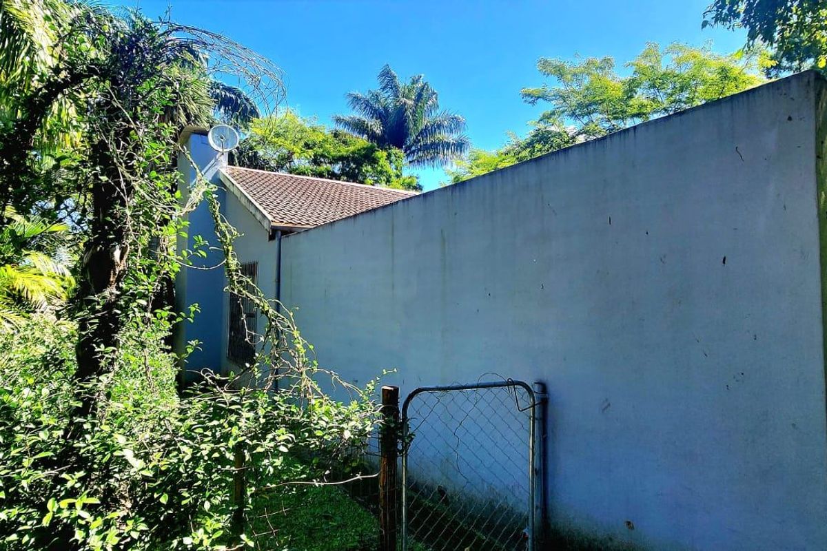 Rear exterior view of the property showing a tiled roof, perimeter wall, and surrounding garden area with mature vegetation.