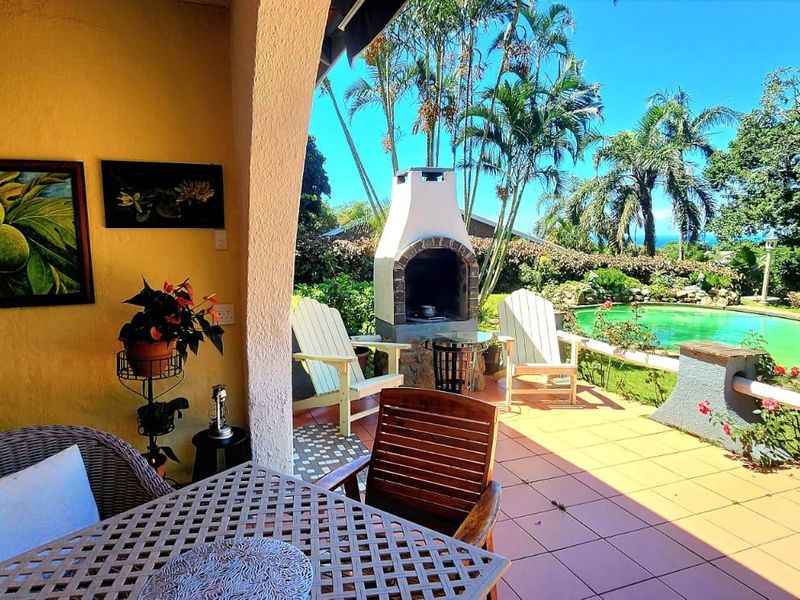Covered patio area featuring a built-in braai, overlooking a private swimming pool and lush landscaped garden.