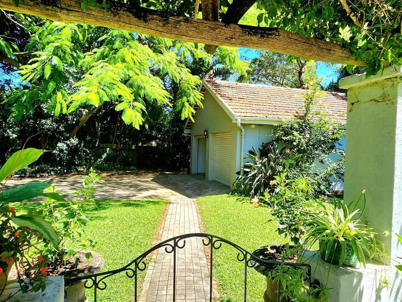 A view of the rear garden featuring a paved walkway leading to a detached garage, framed by a pergola and mature greenery.